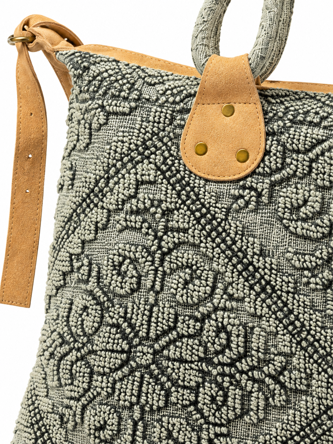 Close-up of a black and ivory textured paisley tote bag featuring raised tufted embroidery, tan suede-look trim, brass-tone rivets, patterned wrapped handles, and an adjustable tan shoulder strap.