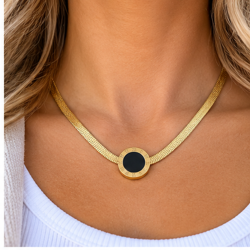 A close-up of a model's neck wearing a gold snake chain necklace with a round bezel-set black center stone.