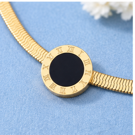 A gold-tone snake chain watch bracelet with a round bezel featuring Roman numerals and a central black inlay, displayed on a textured blue surface.