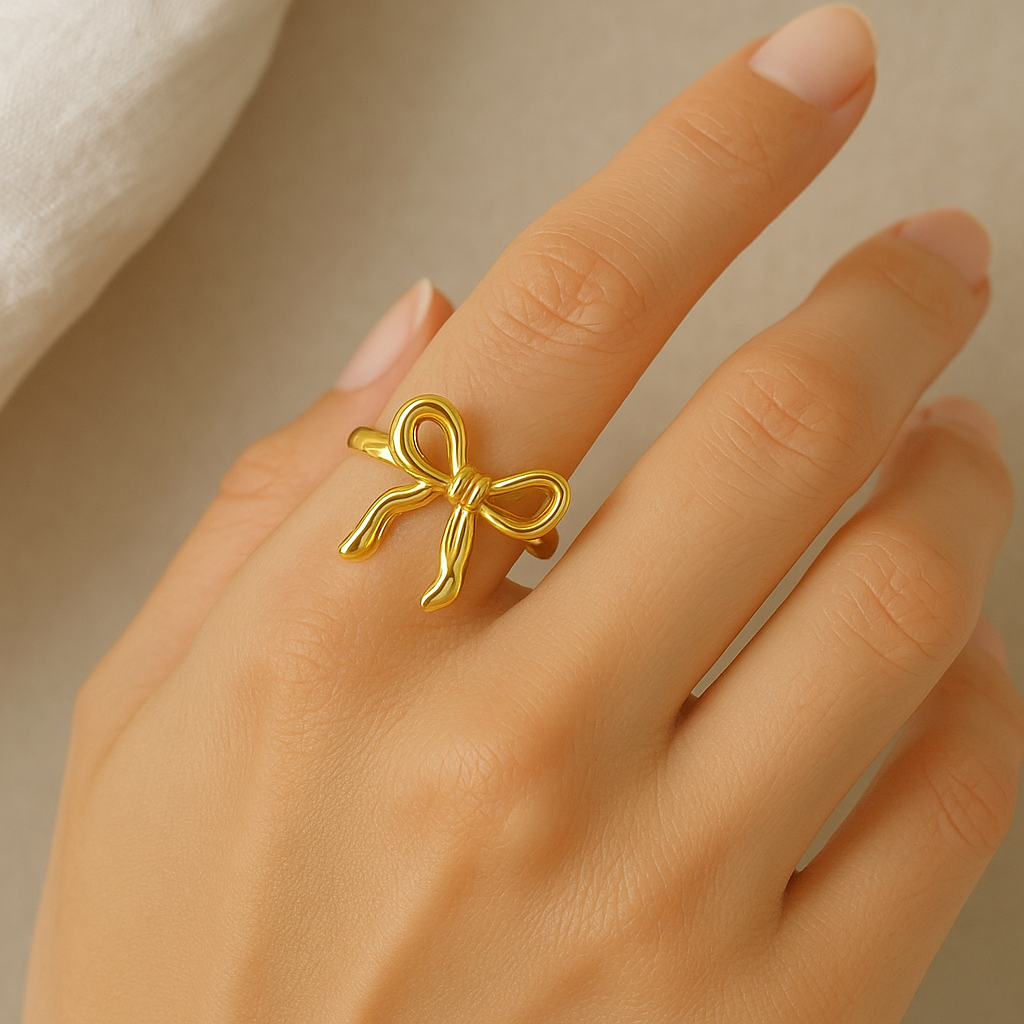 Gold bow-shaped ring on a hand against a neutral background