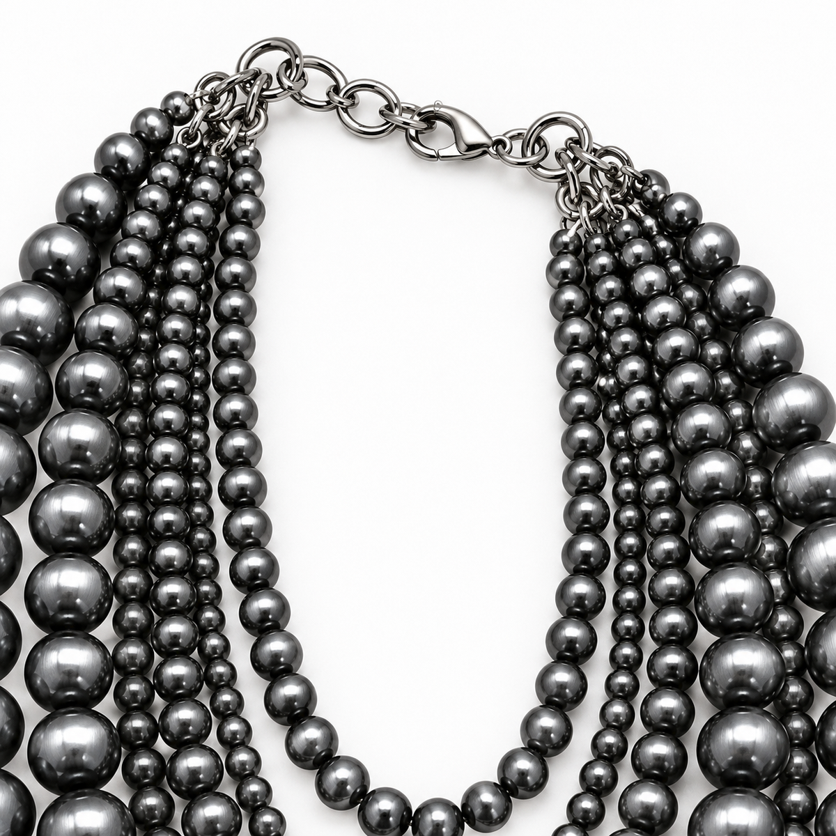 A multi-strand necklace featuring dark gray to black metallic pearls on varying strand lengths, connected by a matching dark metal chain and lobster clasp, shown on a plain white background.