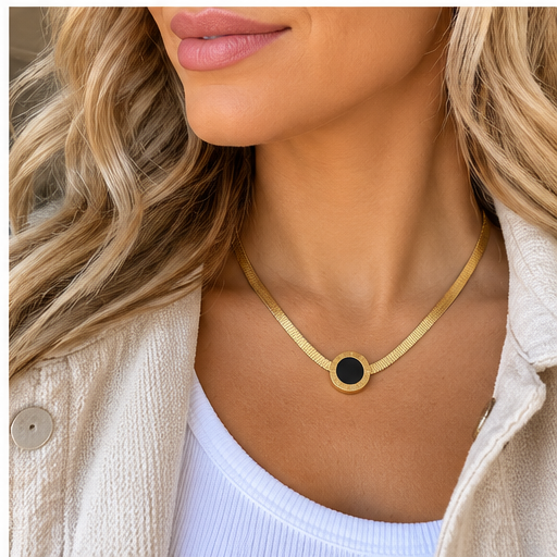 A close-up lifestyle shot of a woman wearing a gold mesh chain necklace with a circular black onyx pendant, styled with a white ribbed tank top and a cream-colored jacket.