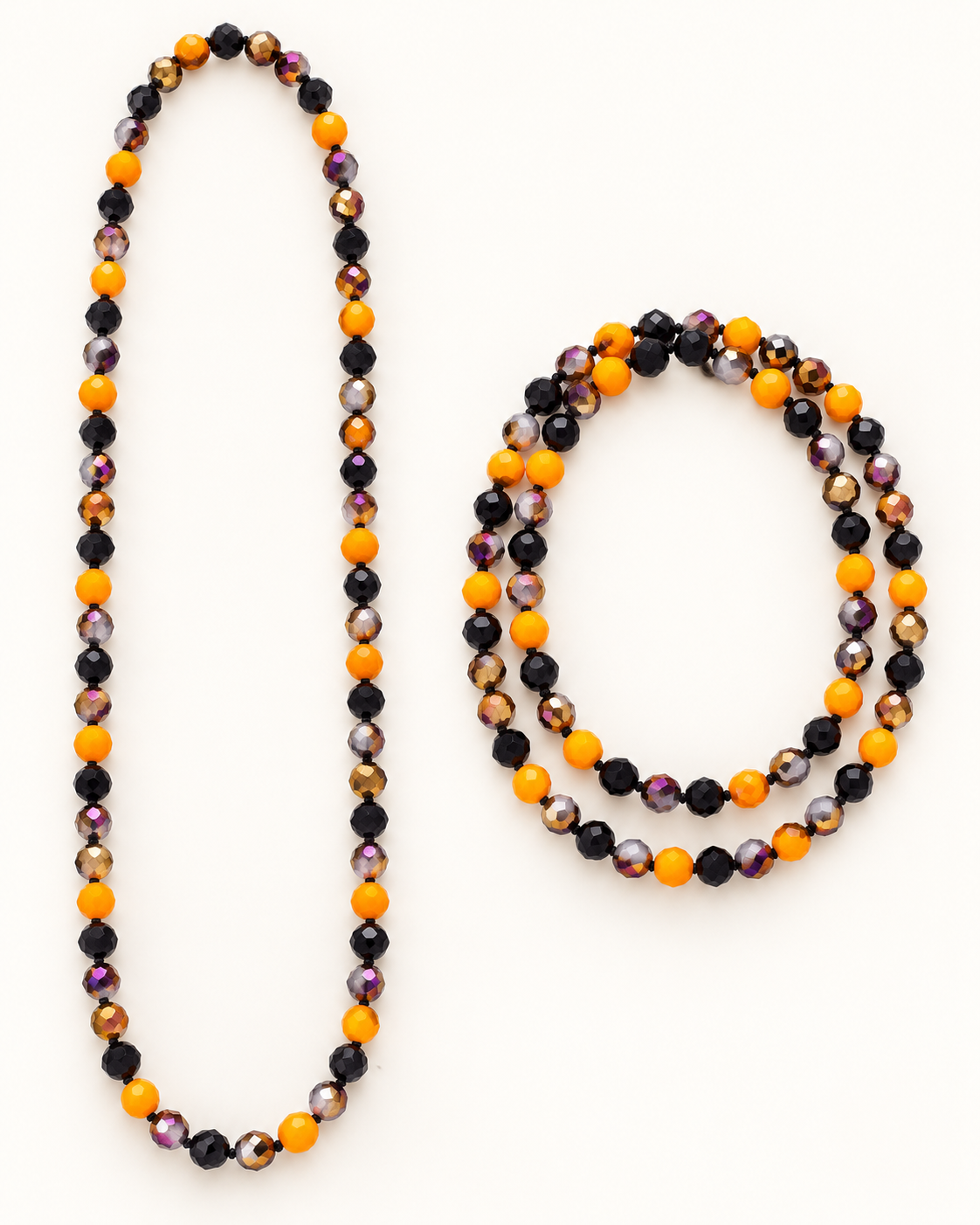 A beaded necklace and matching beaded bracelet laid out on a plain white background. The beads alternate between glossy black, bright orange, and translucent iridescent beads that shift between purple, gold, and brown.