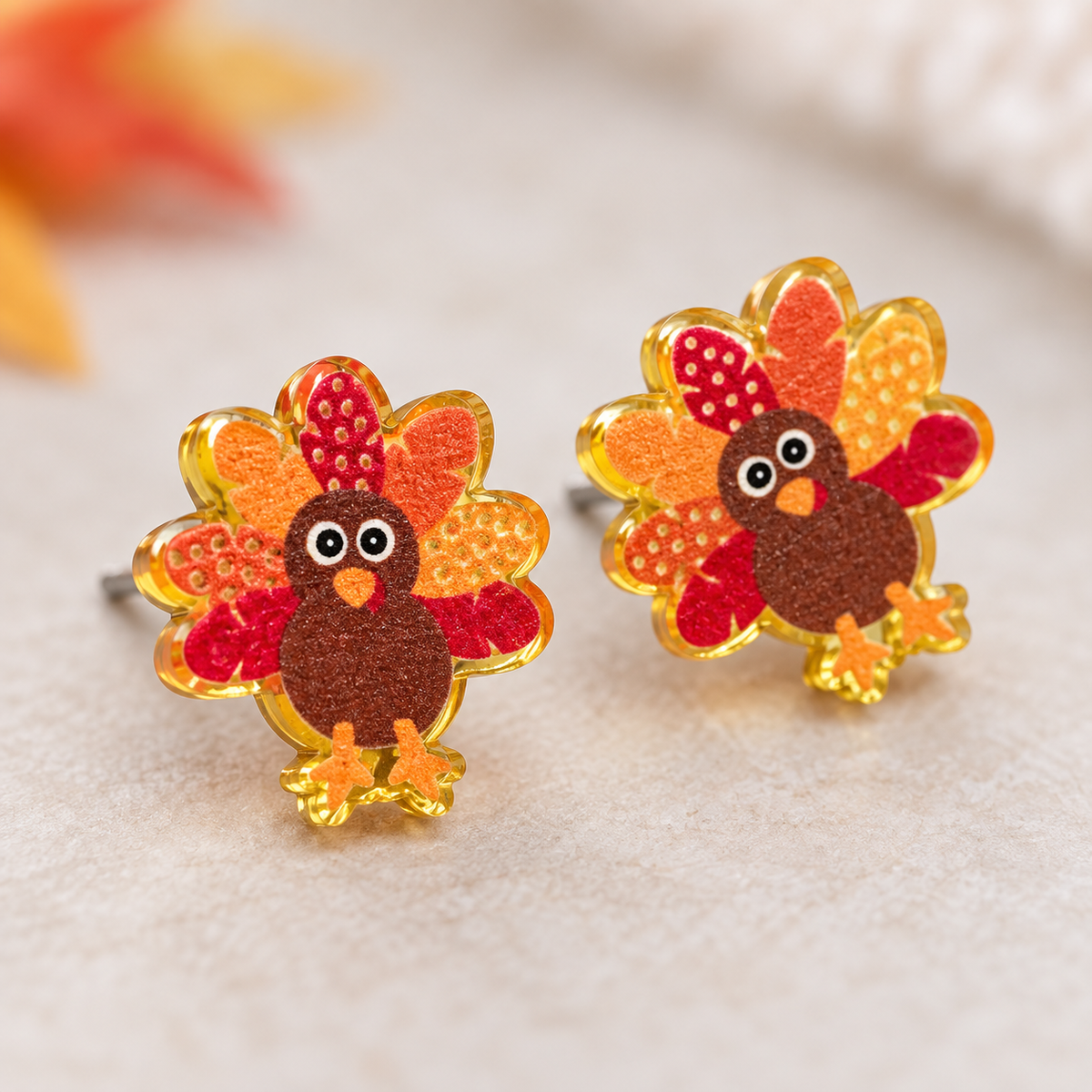 Close-up of small turkey acrylic stud earrings with orange, red, and gold feather details
