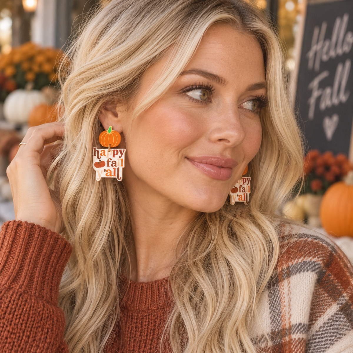Blonde woman wearing Happy Fall Y’all pumpkin statement earrings with rust sweater and plaid fall layers