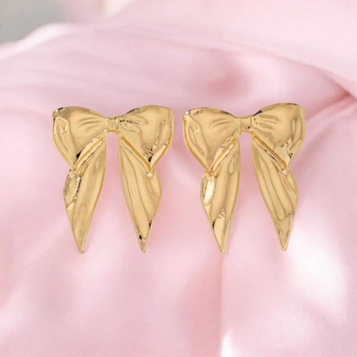 Gold bow-shaped earrings on a pink background