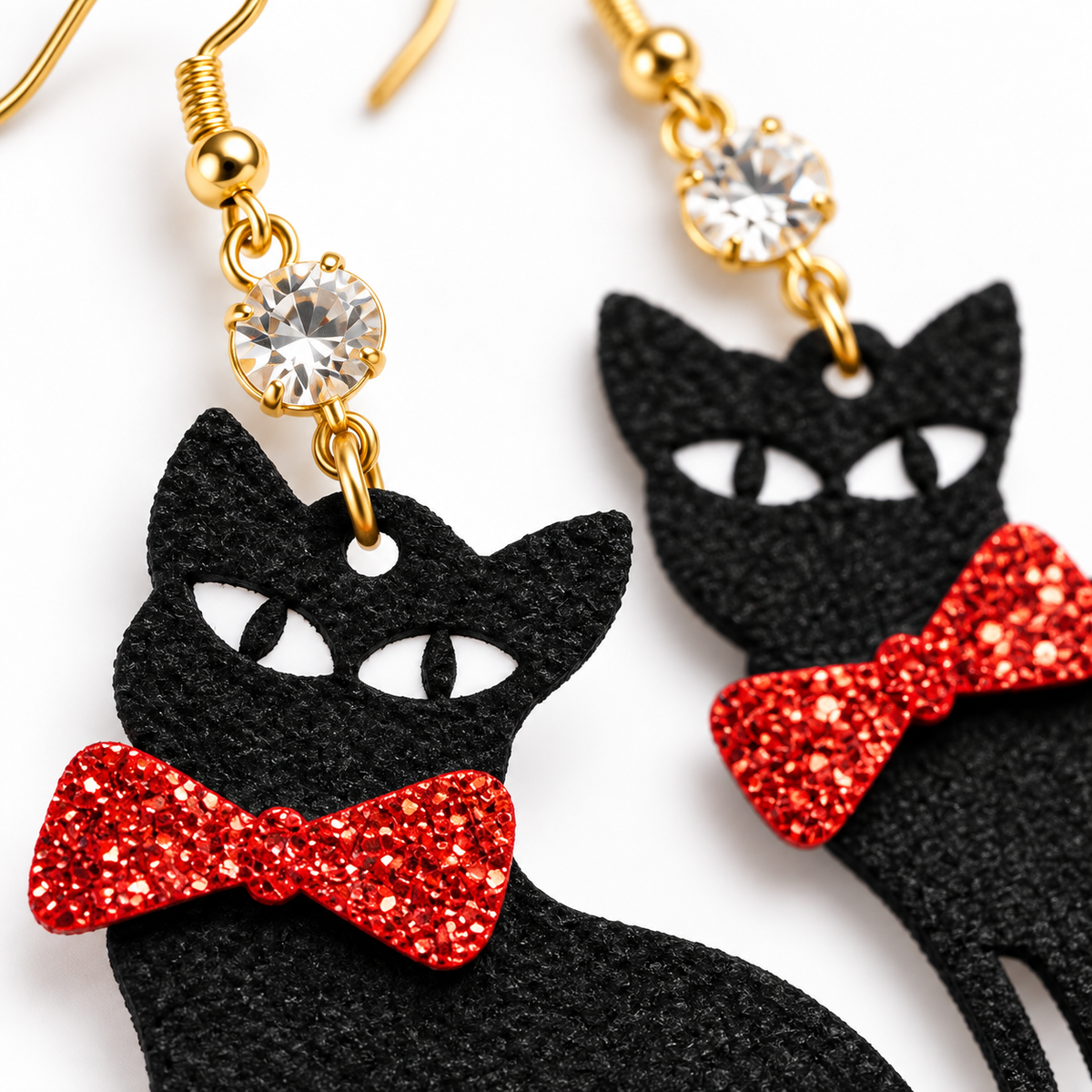Black cat-shaped dangling earrings with white eyes and red glitter bow ties, attached to gold hooks with clear rhinestone accents, shown on a white background.