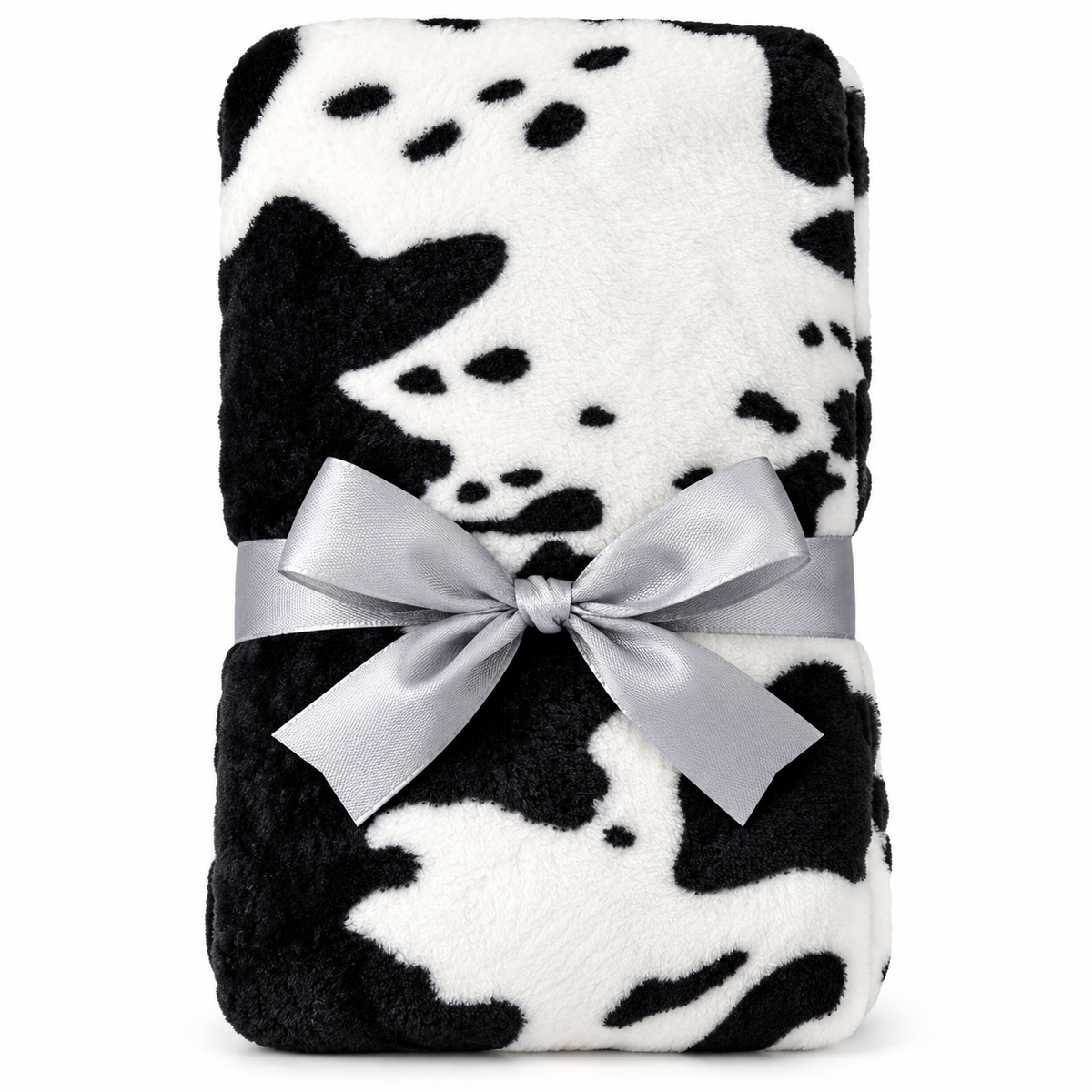 A folded plush blanket with a black and white cow print pattern, wrapped with a wide silver satin ribbon tied in a bow, on a plain white background.