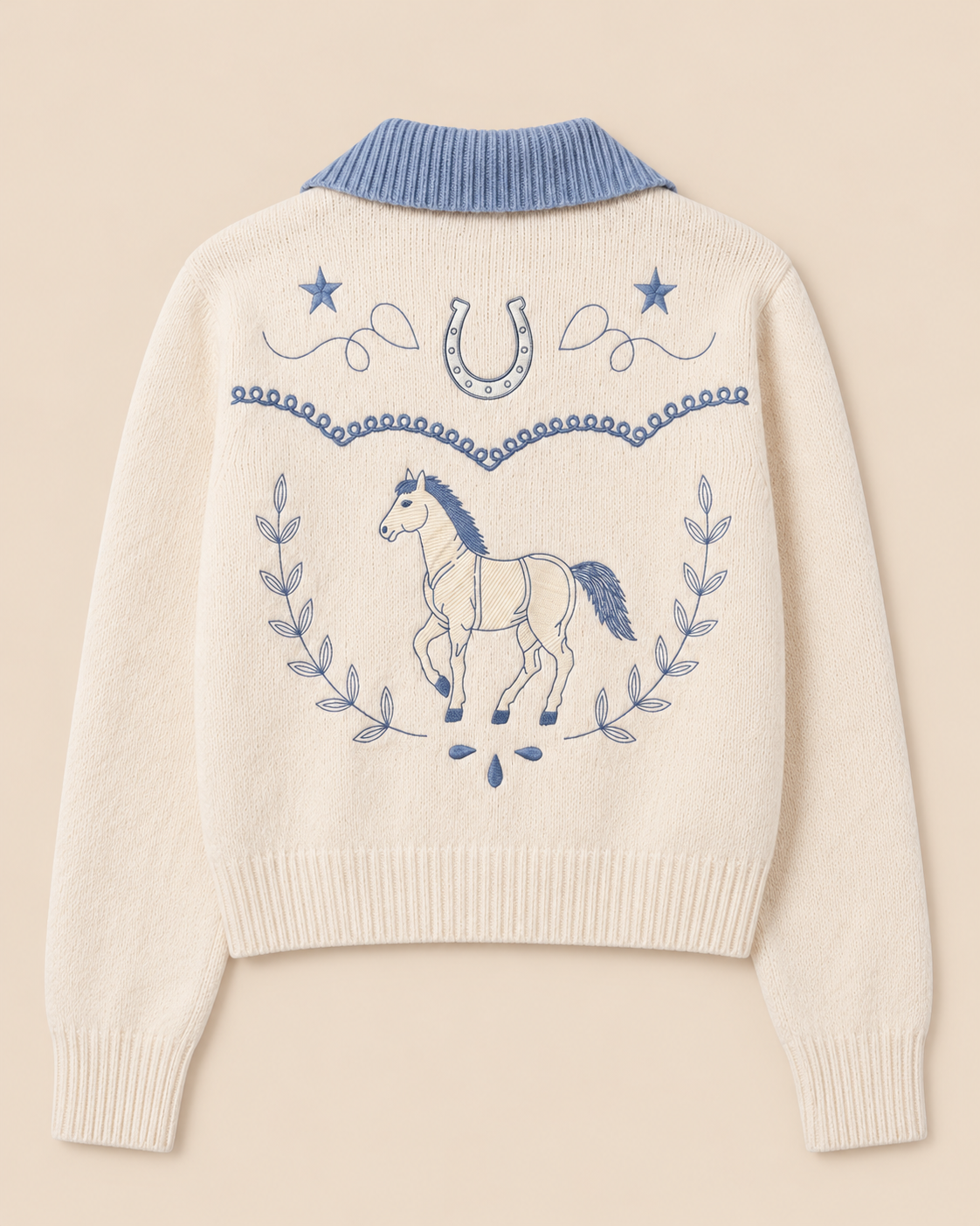 An off-white knit sweater with a light blue ribbed mock neck collar, featuring a blue embroidered design on the back with a horse, stars, a horseshoe, and laurel leaves, shown against a solid beige background.