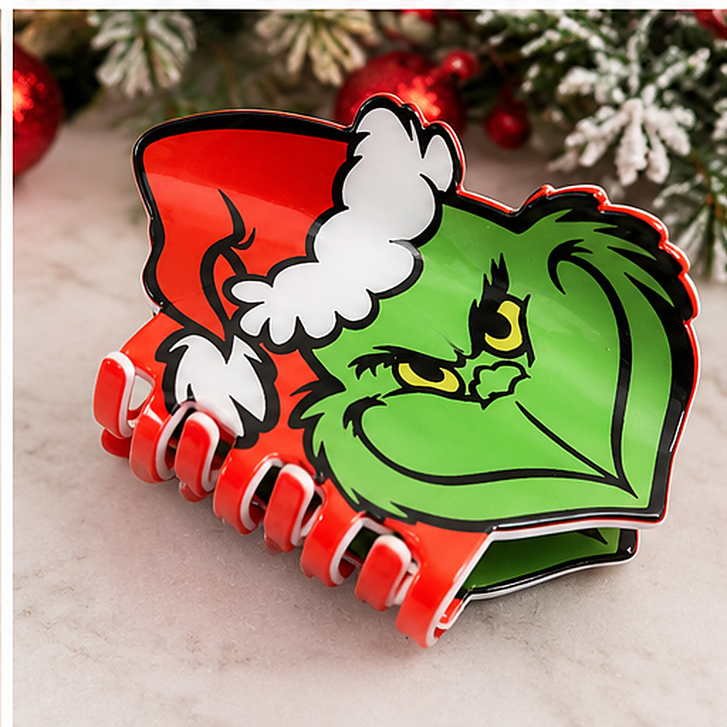 A novelty hair claw clip featuring a cartoon Grinch face wearing a Santa hat, with red and green as the dominant colors, set against a festive holiday background.