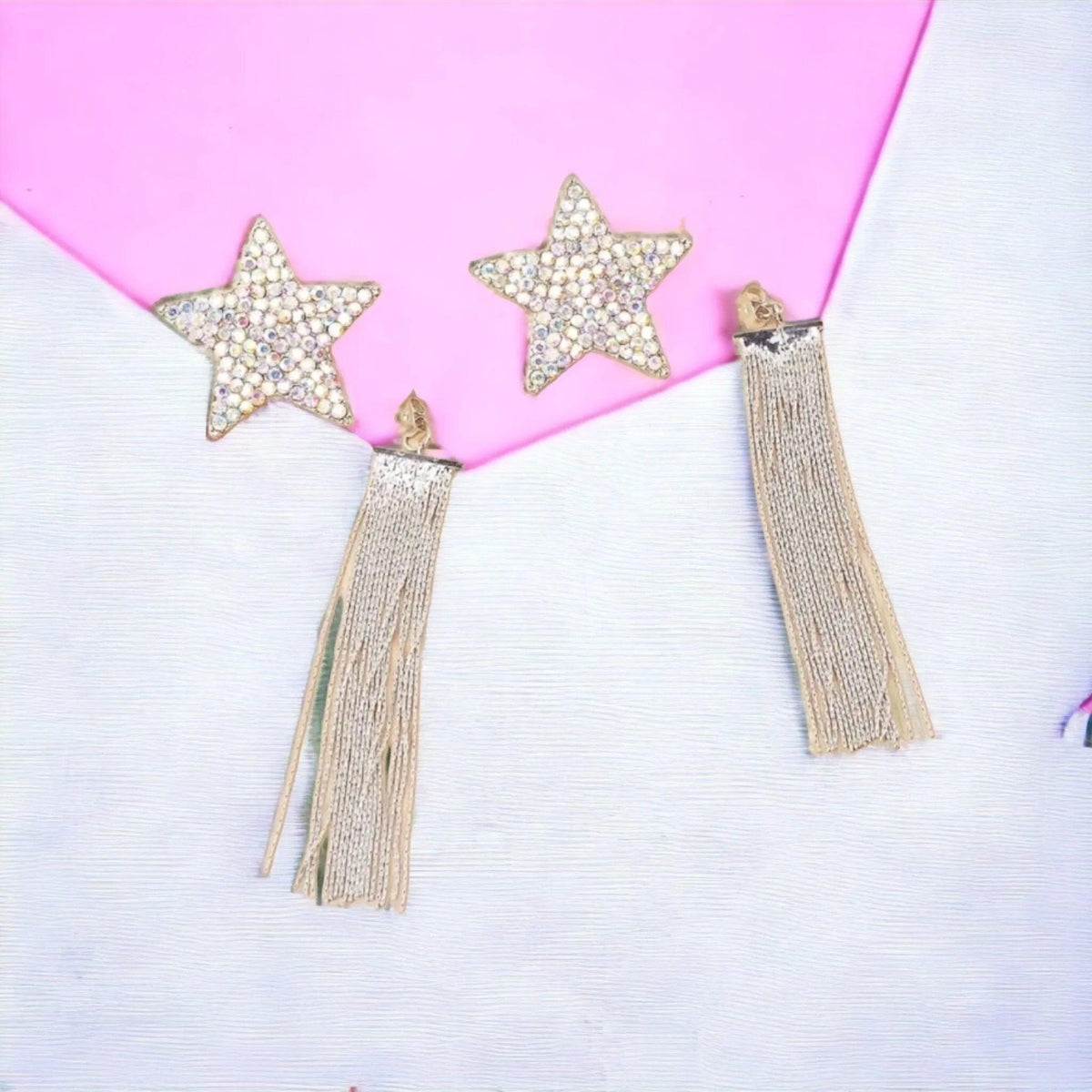 Star-shaped earrings with tassels on a pink and white background