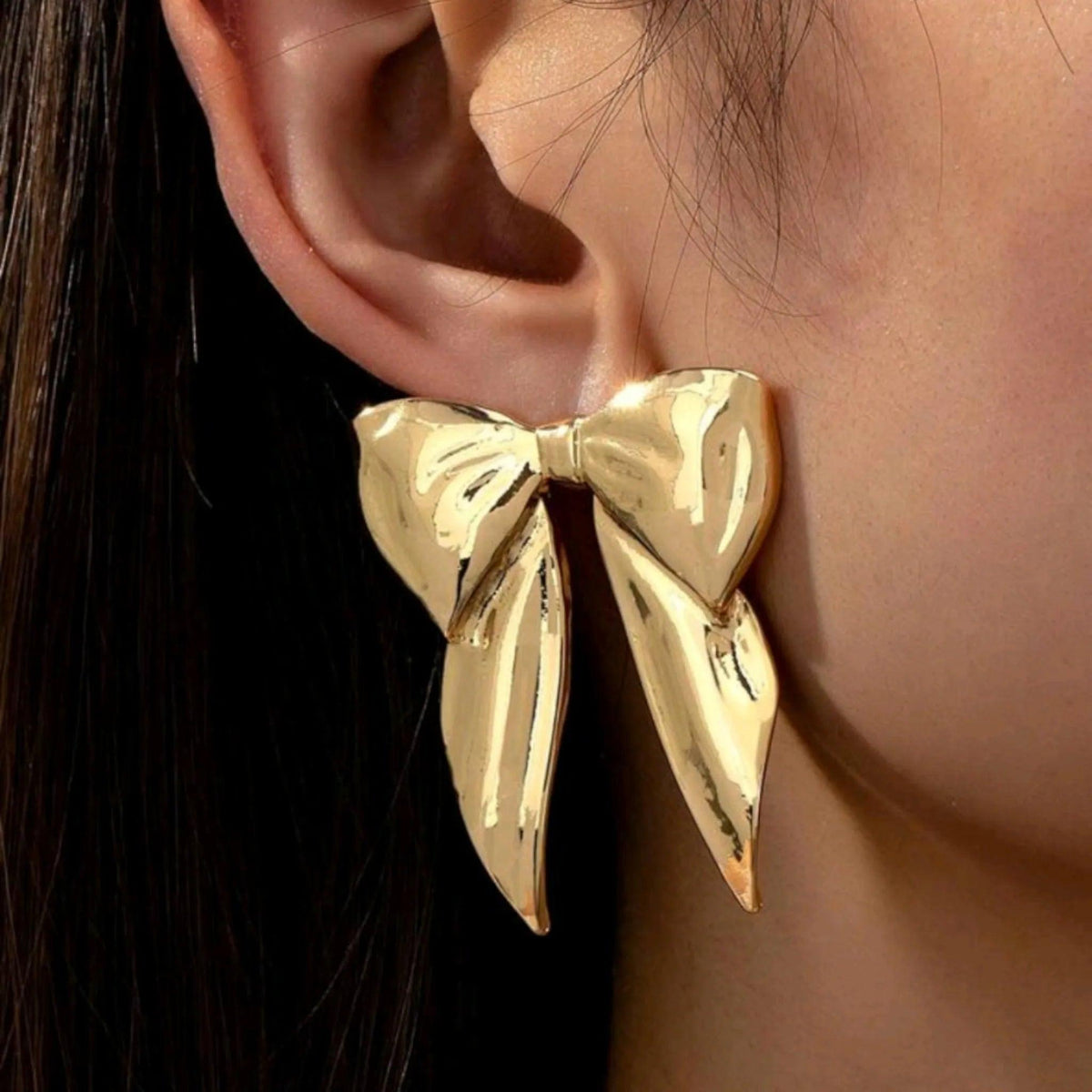 Gold bow-shaped earring worn by a person