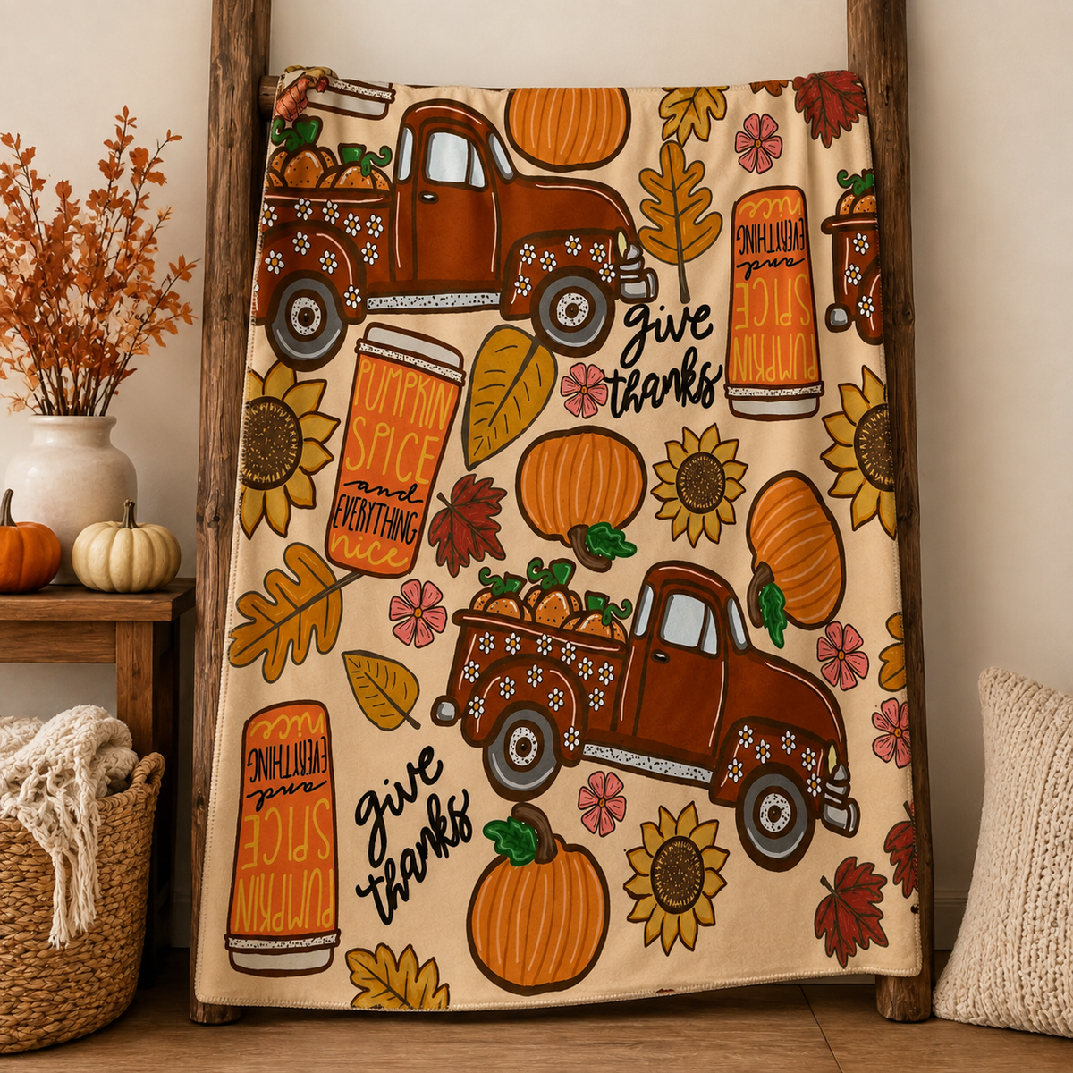 Fall throw blanket styled across a warm neutral bed with pumpkins, trucks, sunflowers and Give Thanks design