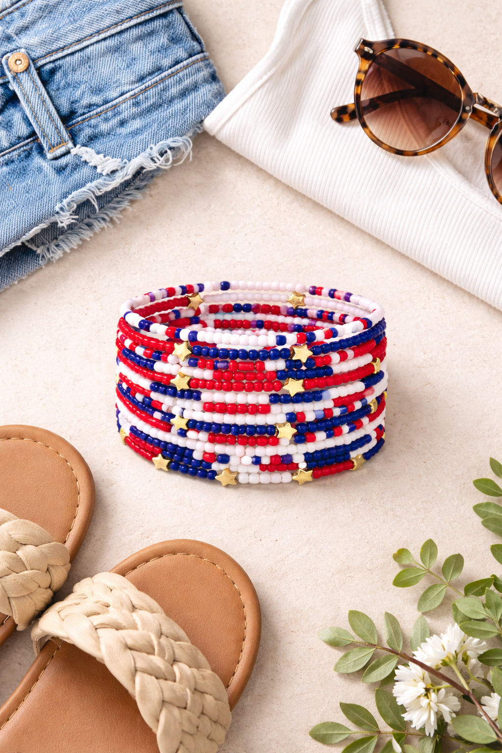 Colorful beaded bracelet on a surface with sandals, sunglasses, and flowers.