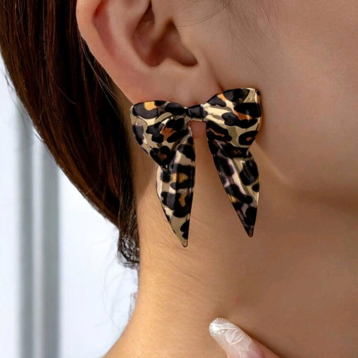 Leopard print bow-shaped earrings worn by a person.