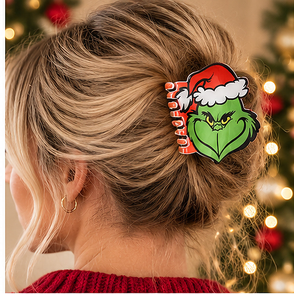 A woman shown from the back with her hair in a bun, wearing a holiday hair clip featuring the Grinch's green face and Santa hat. The background shows a softly blurred Christmas tree with warm lights.