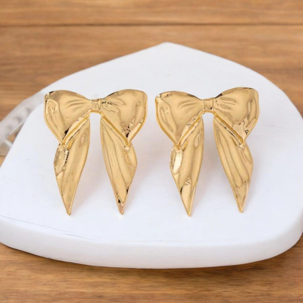Gold bow-shaped earrings on a white stand with a wooden background