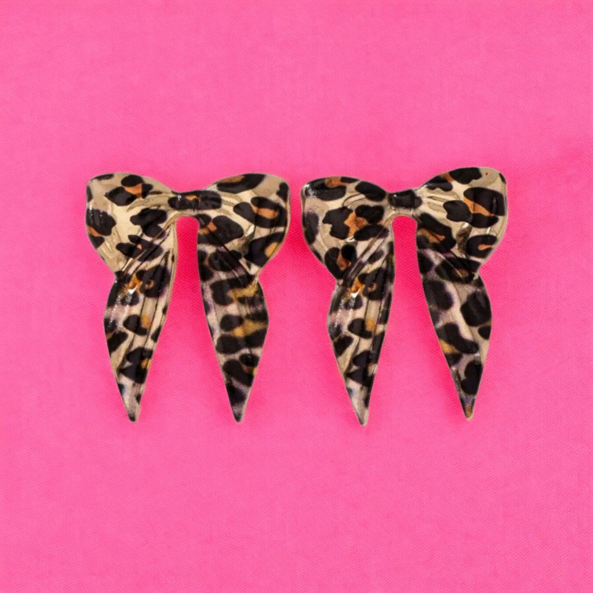 Two leopard print hair bows on a pink background