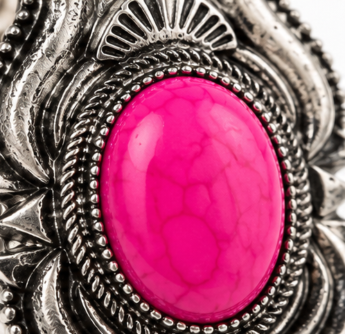 A close-up of a silver-toned ring featuring a large, oval, vibrant hot pink cabochon stone with natural vein-like cracks.