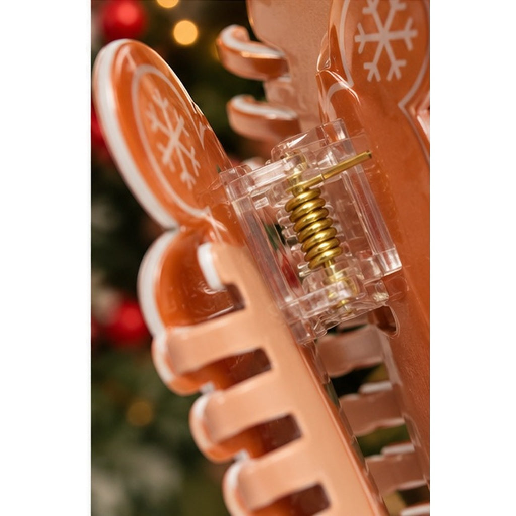 A close-up of a peach-colored hair claw clip decorated with white snowflake patterns, featuring a clear plastic frame and a gold metal spring.
