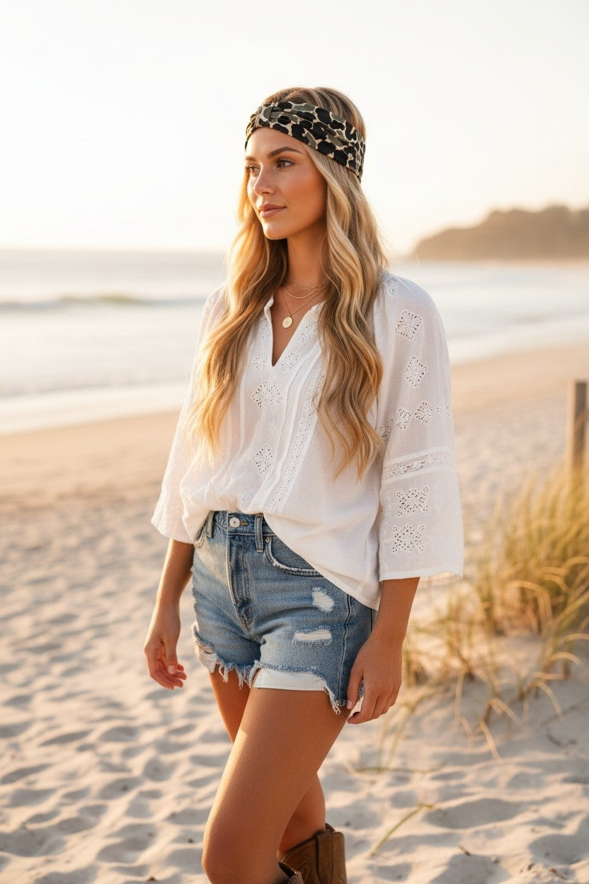 Woman on a beach wearing a white blouse, denim shorts, and a headband with a leopard print design.