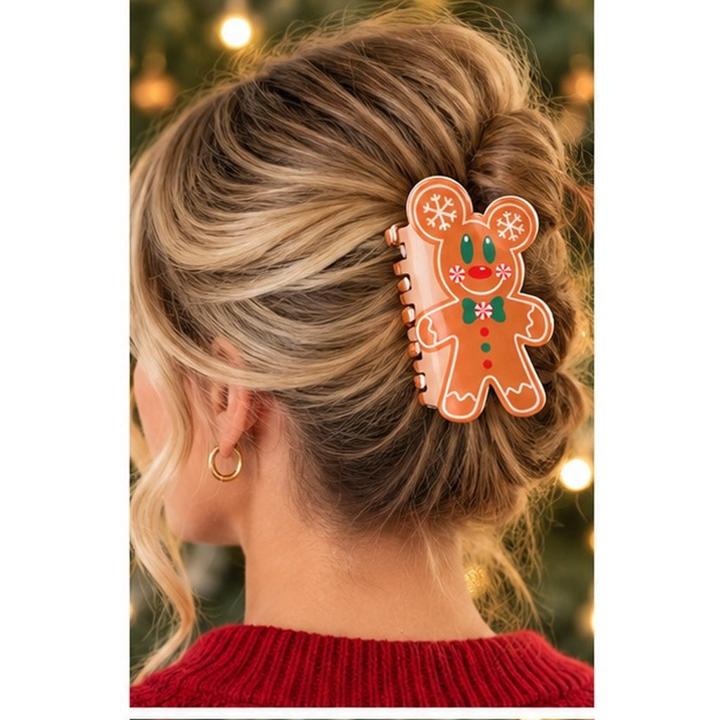 A woman shown from the back with blonde-highlighted hair in a bun, wearing a gingerbread man hair clip in her hair. The clip is light brown with white icing details, red accents, and a green scarf.
