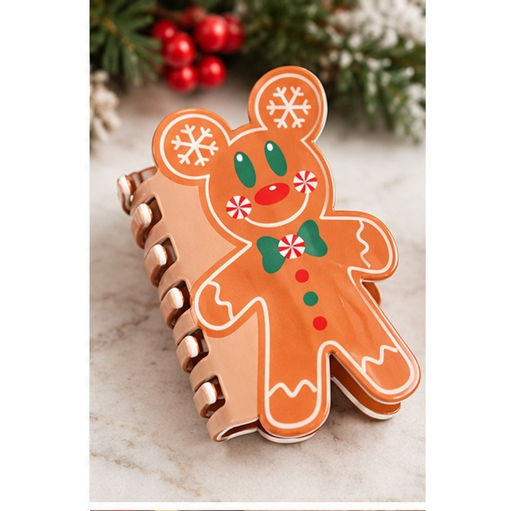 A spiral-bound notebook with a gingerbread man cover, decorated with white icing-style outlines, green eyes and bow tie, and red candy accents, set against a holiday background with pine branches and red berries.
